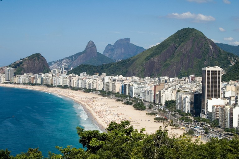 Une vue surélevée sur la plage de Copacabana avec du sable doré, une mer bleue, des bâtiments urbains et des montagnes à Rio de Janeiro.