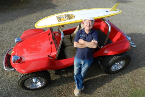 Bruce Myers, inventor of the buggy, leans against his buggy with his surfboard strapped on top. 