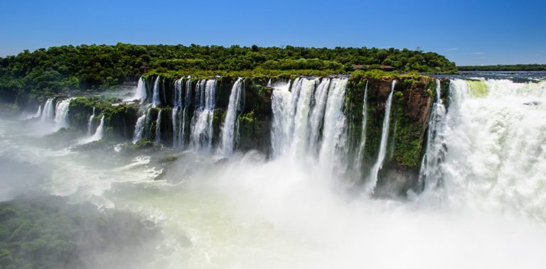 Les chutes d'Iguazú au sud du Brésil, un rideau d'eau majestueux entouré d'une forêt luxuriante sous un ciel bleu clair.