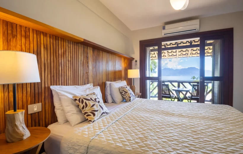 Chambre avec décoration en bois naturel à la Pousada Naturália na Ilha Grande, comprenant un balcon privé avec vue panoramique sur la mer et les montagnes.