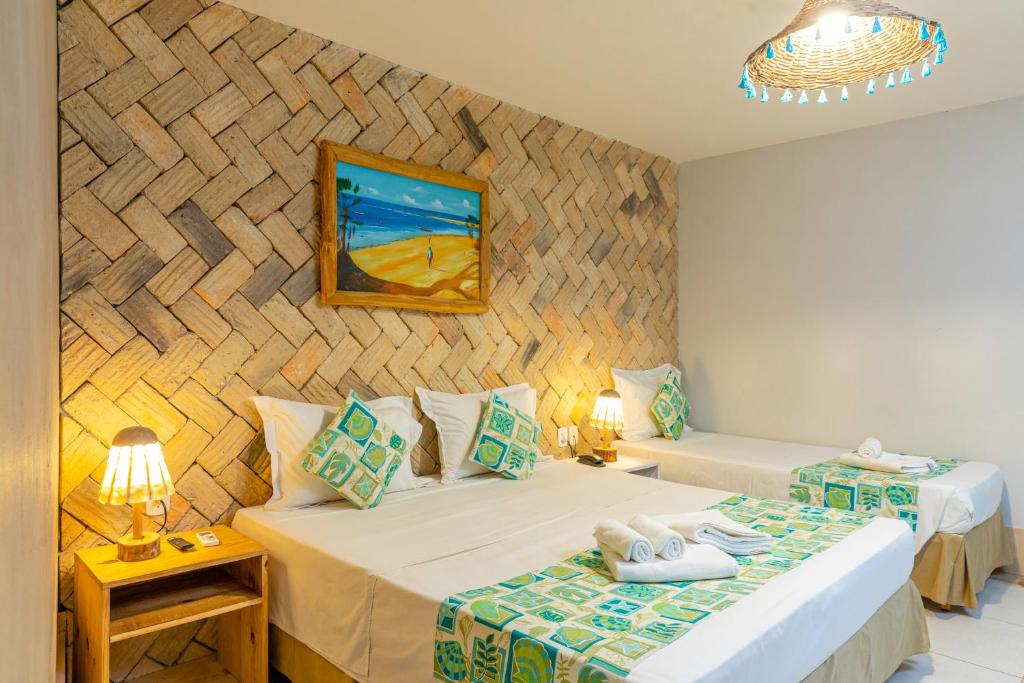 Photographie d'une chambre triple de luxe à la Pousada Vila Parnaíba. L'image montre un grand lit double et un lit simple devant un mur d'accent en briques de terre cuite. La décoration est rustique-chic, avec des touches de turquoise et de vert sur les textiles. Des lampes au design vintage et un lustre en paille éclairent la pièce, qui comprend également un tableau représentant une plage.