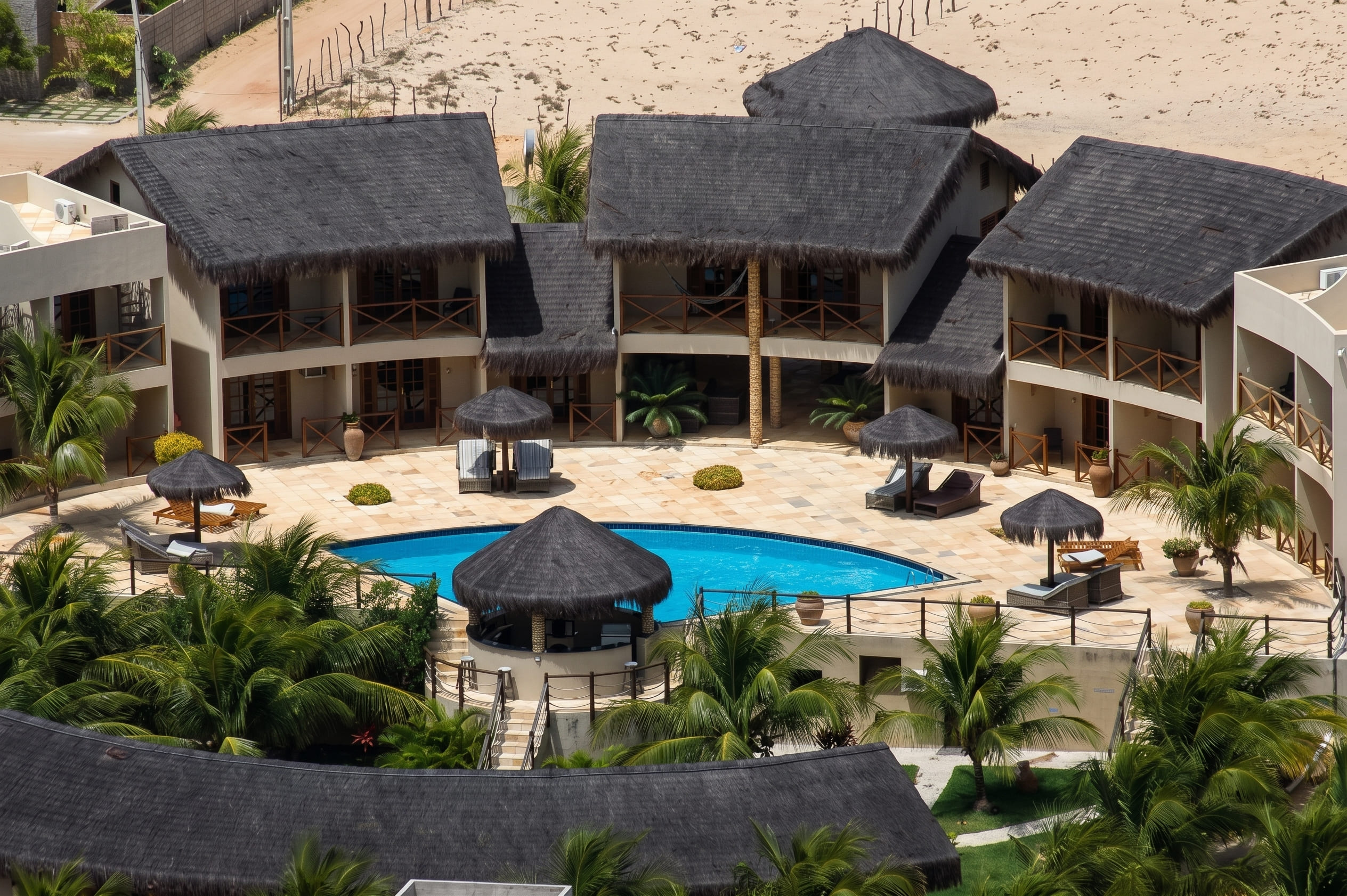 Vue aérienne de l'Aruanã Pousada à Canoa Quebrada, Ceará, Brésil. complexe hôtelier au toit de chaume, piscine bleue, palmiers, chaises longues, plage de sable blanc et océan Atlantique sous un ciel ensoleillé.
