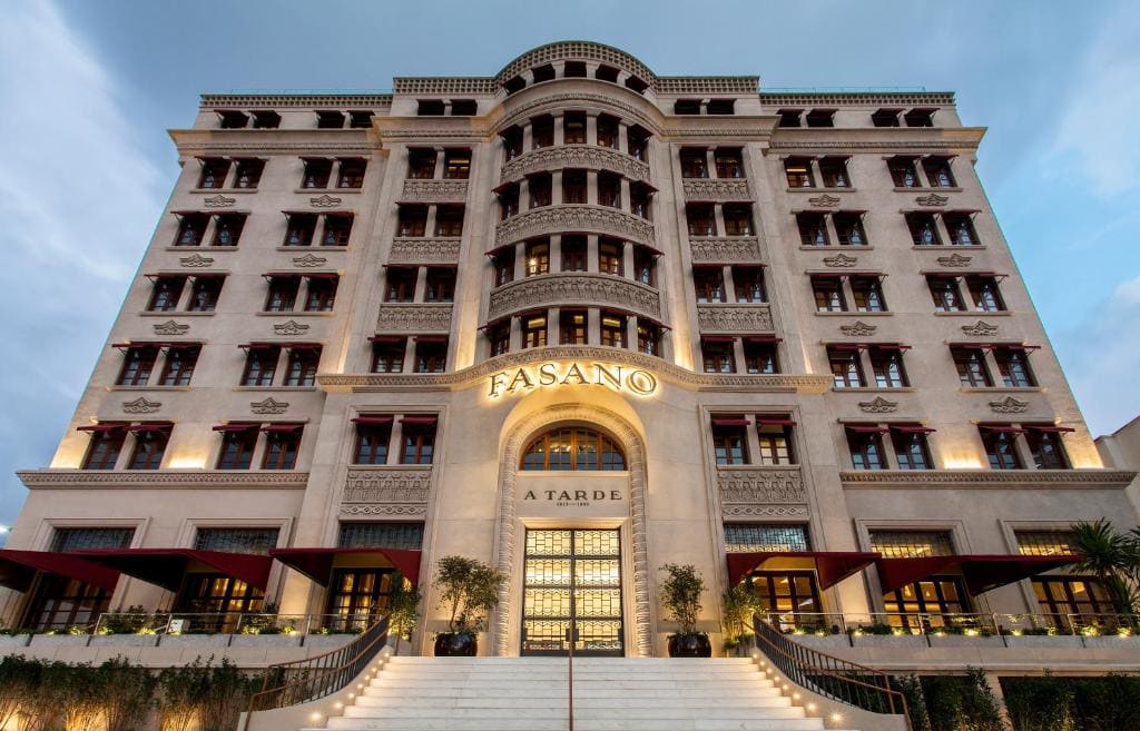 Façade historique illuminée de l'hôtel de luxe Fasano à Salvador, avec son architecture Art déco, une grande entrée voûtée marquée "A Tarde" et un grand escalier menant au bâtiment.