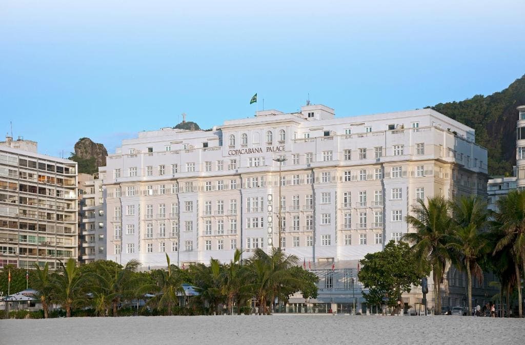 Façade blanche et colonnades historiques de l'hôtel de luxe Copacabana Palace, bordées de palmiers et vues depuis la plage de Copacabana.