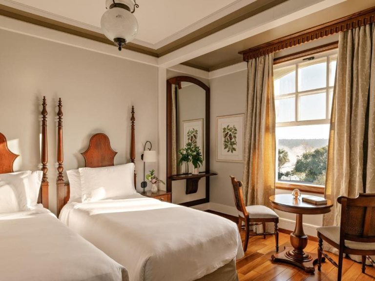Intérieur d'une chambre d'hôtel élégante avec deux lits jumeaux, des têtes de lit en bois sculpté et une fenêtre donnant sur les chutes d'Iguaçu.
