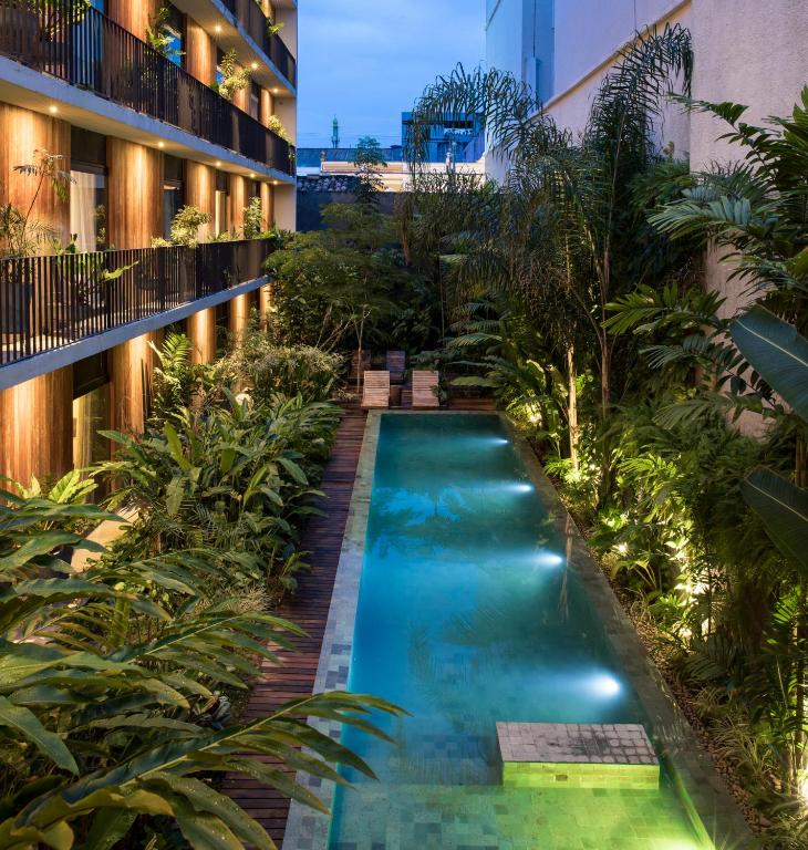http://La%20cour%20intérieure%20de%20l’hôtel%20Vila%20Amazônia%20à%20Manaus,%20au%20crépuscule,%20vue%20d’un%20angle%20surélevé.%20Une%20longue%20piscine%20éclairée%20est%20entourée%20d’une%20végétation%20tropicale%20luxuriante,%20de%20palmiers%20et%20d’un%20deck%20en%20bois%20avec%20des%20transats.%20À%20gauche,%20les%20balcons%20éclairés%20sur%20plusieurs%20étages%20du%20bâtiment%20de%20l’hôtel,%20construits%20en%20bois%20et%20métal%20foncé,%20surplombent%20ce%20jardin%20intérieur.