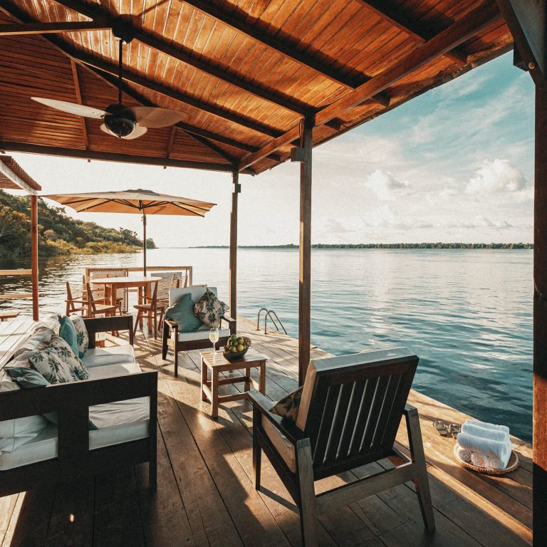 Deck flottant en bois aménagé avec canapés de luxe, parasol et vue panoramique sur le Rio Negro à l'Anavilhanas Jungle Lodge.